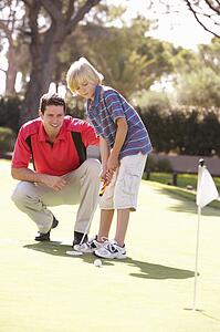 Father Teaching Son To Play Golf On Putting On Green