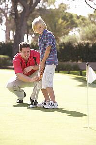 Father Teaching Son To Play Golf On Putting On Green