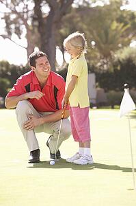 Father Teaching Daughter To Play Golf On Putting On Green