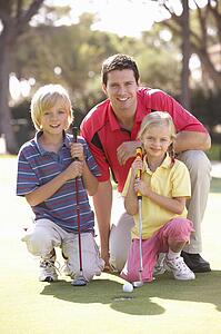Father Teaching Children To Play Golf On Putting On Green