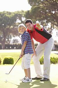 Father Teaching Son To Play Golf On Putting On Green