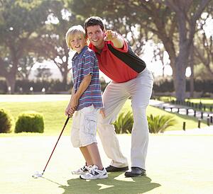 Father Teaching Son To Play Golf On Putting On Green