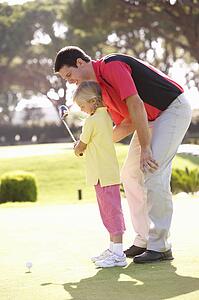 Father Teaching Daughter To Play Golf On Putting On Green