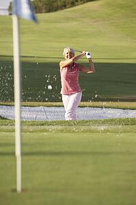 Senior Female Golfer Playing Bunker Shot On Golf Course