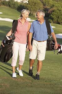 Senior Couple Walking Along Golf Course Carrying Bags