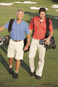 Two Men Walking Along Golf Course Carrying Bags
