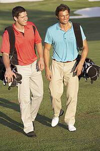 Two Men Walking Along Golf Course Carrying Bags