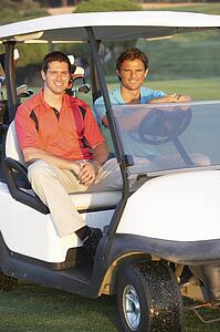 Two Male Golfers Riding In Golf Buggy On Golf Course
