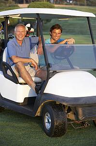 Two Male Golfers Riding In Golf Buggy On Golf Course