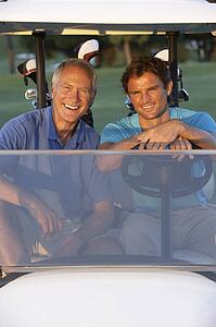 Two Male Golfers Riding In Golf Buggy On Golf Course