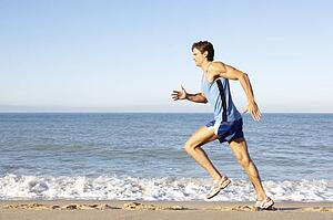 Young Man In Fitness Clothing Running Along Beach