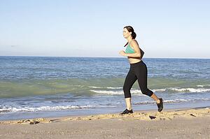 Young Woman In Fitness Clothing Running Along Beach