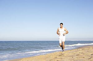 Young Man In Fitness Clothing Running Along Beach