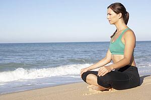 Young Woman In Fitness Clothing Meditating On Beach
