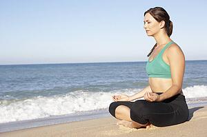 Young Woman In Fitness Clothing Meditating On Beach