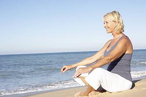 Senior Woman In Fitness Clothing Meditating On Beach