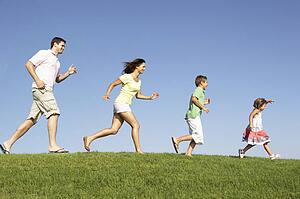 Young family, parents with children, running through field