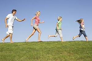 Young family, parents with children, running through field