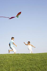 Young children run with kite through field