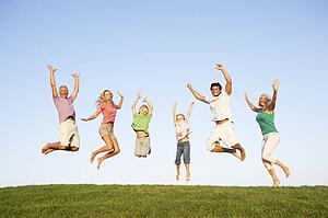 Young couple with grandparents and children jump in a field