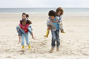 Happy children playing piggyback on beach