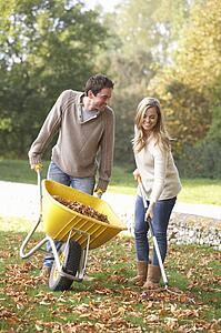 Young couple raking autumn leaves in garden