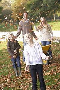 Family throwing autumn leaves into the air in garden