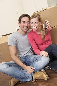 Young couple sit on the floor around boxes holding key in hand
