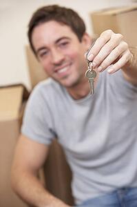 Young man sits on the floor around boxes holding a key in his hand