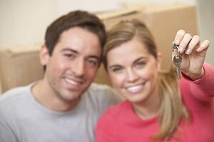Young couple sit on the floor around boxes holding key in hand