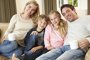 Happy young family sitting on sofa holding cups