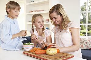 Young mother with children peeling vegetables in kitchen