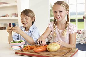Happy children peeling vegetables in kitchen