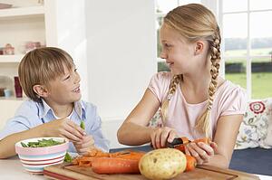 Happy children peeling vegetables in kitchen