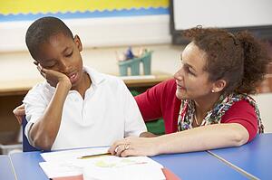 Unhappy Schoolboy Studying In Classroom With Teacher