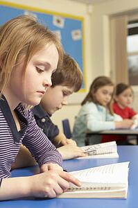 Schoolgirl Reading Book In Classroom