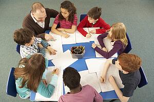 Overhead View Of Schoolchildren Working Together At Desk With Teacher