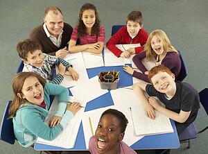 Overhead View Of Schoolchildren Working Together At Desk With Teacher