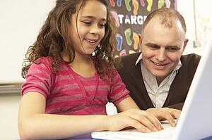 Schoolgirl In IT Class Using Computer With Teacher
