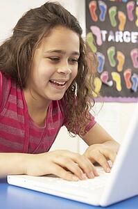 Schoolgirl In IT Class Using Computer With Teacher