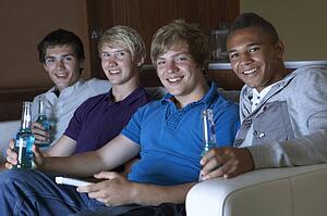 Group Of Teenage Boys Sitting On Sofa At Home Watching Drinking Alcohol