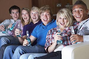 Group Of Teenage Friends Sitting On Sofa At Home Watching Drinki