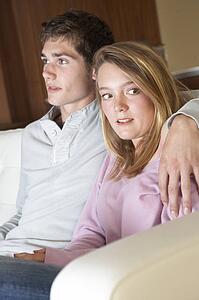 Nervous Looking Teenage Girl Sitting On Sofa At Home With Boyfri