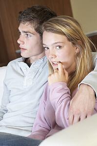Nervous Looking Teenage Girl Sitting On Sofa At Home With Boyfri