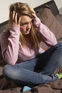 Depressed Teenage Girl Sitting In Bedroom At Home