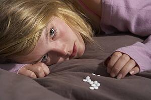 Depressed Teenage Girl Sitting In Bedroom With Pills