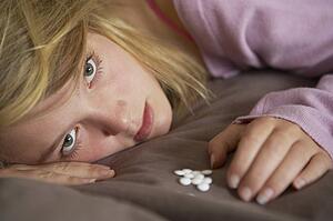 Depressed Teenage Girl Sitting In Bedroom With Pills