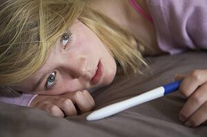 Depressed Teenage Girl Sitting In Bedroom With Pregnancy Test