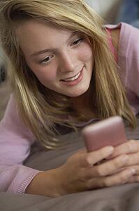 Teenage Girl Lying In Bedroom Using Mobile Phone