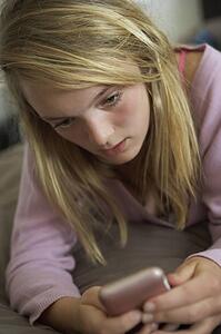 Unhappy Teenage Girl Lying In Bedroom With Mobile Phone
